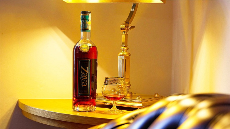 Rum Zaya Gran Reserva s koňakovou sklenkou pod stolní lampou