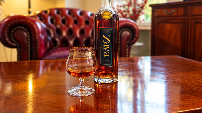 Lahev rumu Zaya Gran Reserva a sklenka na stole v salonku s koženou sedačkou